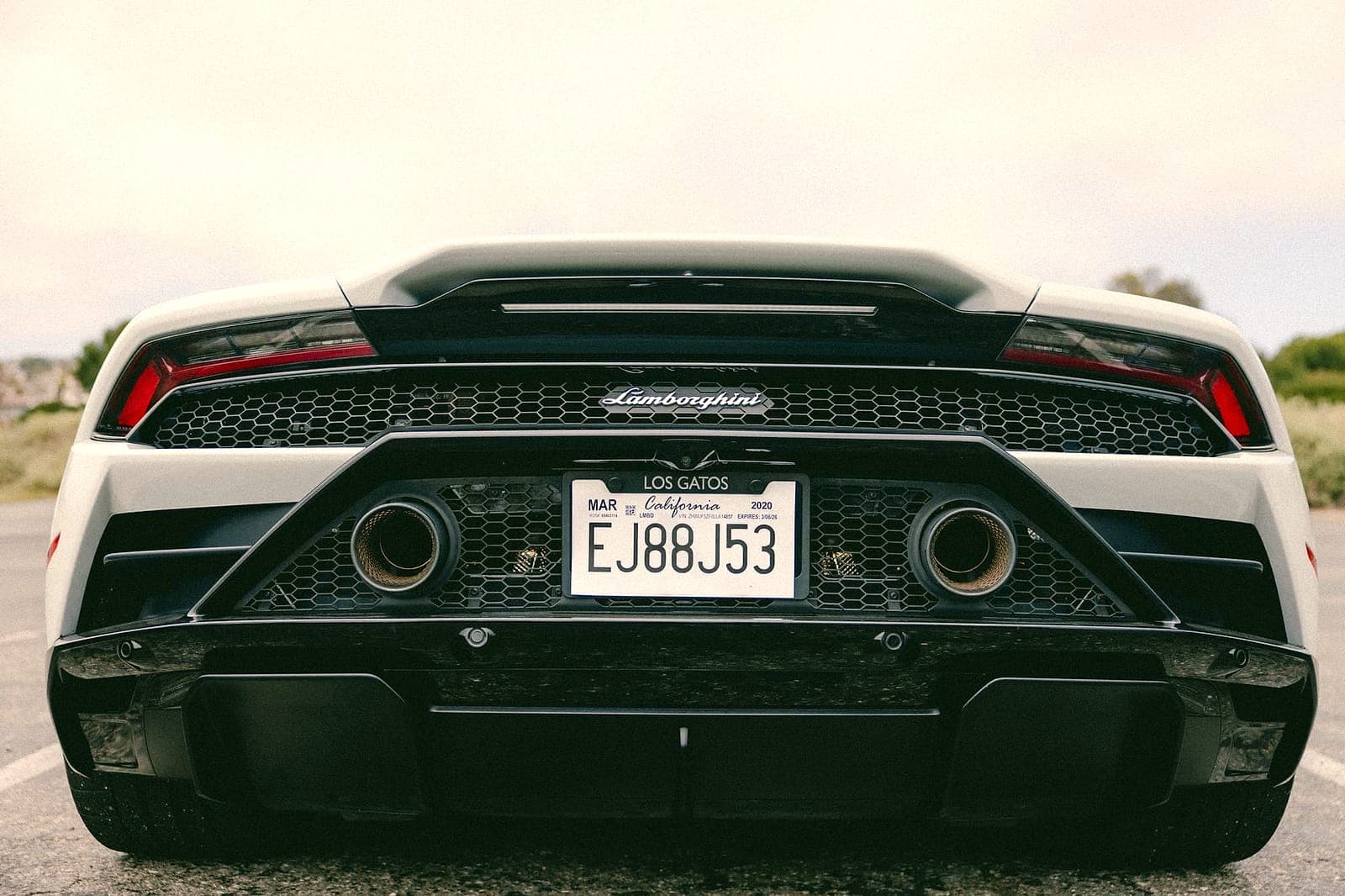 White Lamborghini Huracán, rear with quad exhaust, in Orange County daylight