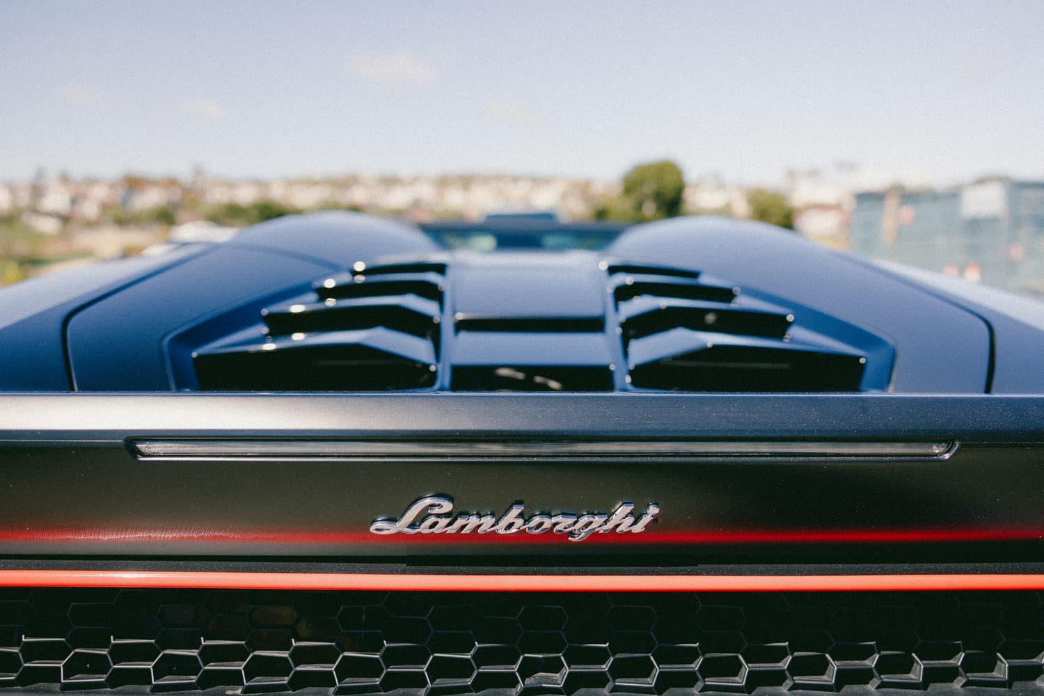 Detail of the Huracán Spyder rear engine deck — black louvered cover, chrome Lamborghini script and a red accent line